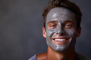 portrait of a smiling happy young man smiling while pampering his skin with a face mask on white background. photo