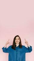 Vibrant Portrait of Energetic Young Woman Expressing Amazement with Open Mouth and Pointing Fingers Upward, Isolated on Pink Background photo
