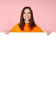 Surprised Woman Holding White Promo Paper for Unexpected Best Deal Offer. Expressive Shock and Excitement. Isolated on Pink Background. Perfect for Advertising, Marketing, and Promotional Concepts photo