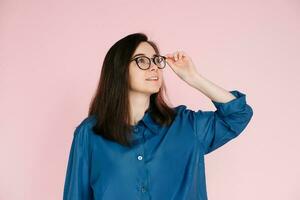 Thoughtful Woman in Glasses, Touching Her Frames, Deep in Contemplation, Searching for Ideas in Empty Space. Isolated Pink Background Portrait photo