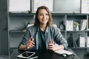 un sofisticado mujer de negocios es atractivo en un vídeo conferencia desde su oficina o hogar. ella es atentamente mirando dentro el web cámara, articular su pensamientos y ideas con claridad y confianza. foto