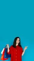 linda mujer en rojo camisa con compras bolso - señalando a vacío espacio - Perfecto para promoviendo ventas y descuentos - aislado en azul antecedentes foto