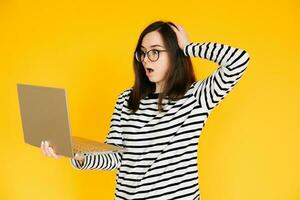 Picture of a cute impressionable lady in a striped T-shirt with glasses, reading the news or writing on a modern laptop device, hand head isolated yellow background color photo