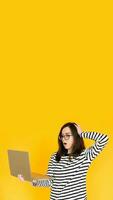 Picture of a cute impressionable lady in a striped T-shirt with glasses, reading the news or writing on a modern laptop device, hand head isolated yellow background color photo