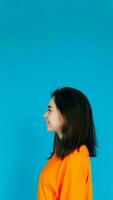 Radiant Young Woman in Stylish Orange Attire Smiling with a Beaming Toothed Smile, Profile Portrait, Isolated on Blue Background photo