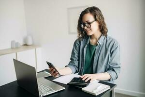 Professional woman accountant working with calculator and laptop computer in office. Smiling businesswoman working remotely from home office. Finance and accounting concept, work-from-home, finance. photo