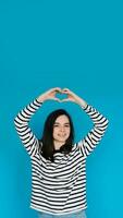 Happy Woman in Striped Sweater Spreading Love and Positivity - Smiling Girl with Raised Arms Forming Heart Shape, Expressing Joy and Affection - Isolated Blue Background - Ideal for Happiness, Love photo