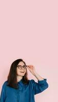 Curious Woman Touching Glasses, Deep in Thought, Searching for Inspiration in Empty Space. Isolated Pink Background Portrait photo