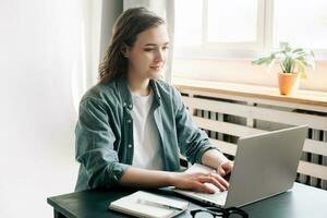 Young woman multitasking with a laptop in a modern office environment and student girl focused on work from home. Online work, study, freelance, business, and office lifestyle concept photo