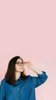 Thoughtful Woman in Glasses, Touching Her Frames, Deep in Contemplation, Searching for Ideas in Empty Space. Isolated Pink Background Portrait photo