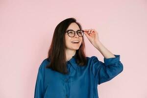 Curious Woman Touching Glasses, Deep in Thought, Searching for Inspiration in Empty Space. Isolated Pink Background Portrait photo