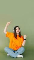 Portrait of a joyful woman wearing headphones, expressing enthusiasm and approval while pointing both thumbs towards empty space, isolated on a vibrant green background photo