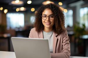 Portrait of a Beautiful Diverse Female Wearing Glasses, Using Laptop Computer, Looking at Camera and Smiling. Information Technology Specialist, Software Engineer or Developer. photo
