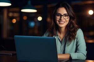 Portrait of a Beautiful Diverse Female Wearing Glasses, Using Laptop Computer, Looking at Camera and Smiling. Information Technology Specialist, Software Engineer or Developer. photo