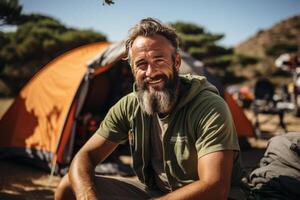 Portrait of pretty senior man in white casuals writing journal besides tent in forest. photo