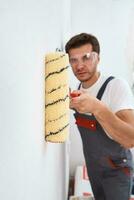 Home renovation concept. Man in uniform painting wall with paint roller photo