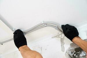 Electrician fixing electric cable to the wall, closeup photo