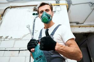 Renovation concept. Man in builder uniform with hammer drill make repairs in the room photo