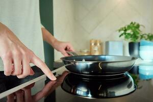 Woman turn on induction hob with frying pan photo