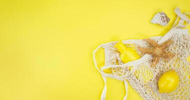 Starfish, shells with bag string with sunscreen bottle mockup and lemon from the side on yellow background. Concept of summer time, vacation, travel. Banner. Copy space photo