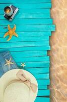 Blue pier boards or sun lounger with shorts, straw hat, starfish and camera next to sea water. Beach layout. Travel, tourism, summer background. Copy space photo