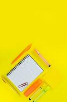 Open chequered notebook with pen, marker and paperclip next to stickers on yellow background. Back to school, drawing. Copy space photo