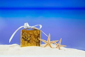 Golden packed gift box with yellow stars at tropical ocean beach. Christmas, New Year, birthday vacation in hot countries background concept. Copy space photo