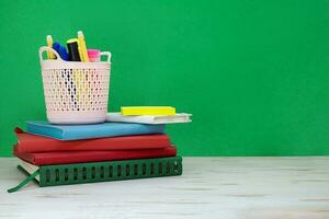 Stack of notepads with pencil case of markers on white table. Green board. Back to school. Copy space photo