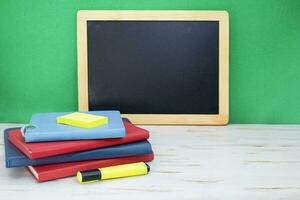 Stack of notepads with marker on white table. Black board on green background. Back to school. Copy space photo