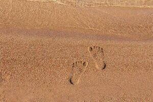 Human footprints on sand of beach near sea coast. Monochrome. Vacation, travel, summer. Steps on shore. Copy space photo