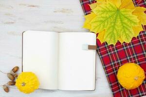 Yellow leaves, red checkered plaid, acorns and empty notebook. Autumn concept, study, work. Copy space photo