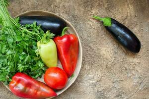 rojo tomate, pimienta, perejil, berenjena mentira en un de madera plato en un marrón antecedentes. ingrediente para cocinando. parte superior vista. Copiar espacio foto