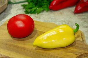 Red tomato, yellow bell pepper on a wooden board. Parsley, cilantro and two red peppers in the back. Ingredient for cooking photo