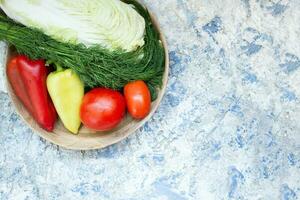 rojo Tomates, amarillo verde y rojo pimientos, eneldo, repollo mentira en un de madera plato en un blanco y azul antecedentes. ingrediente para cocinando. ver desde arriba. Copiar espacio foto