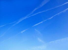 The background is pure blue sky with soft transparent clouds. Trace of the plane. photo