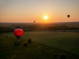 Colorful air balloon is flying in free flight over the field. Bird's-eye view. Multicolored balloon in the sky at sunset photo