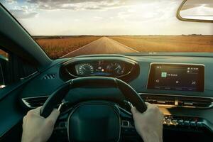 Driving car through a perfect road. Fields illuminated by sunrays. First person view. Modern car with displays on dashboard photo