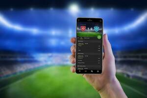 Soccer betting online app on smart phone ih man hand with football stadium in background photo