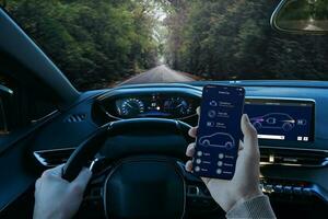 Driver uses the smart car appwhile driving, in order to read the parameters of the car. First person view of car cockpit and smart phone in hand photo