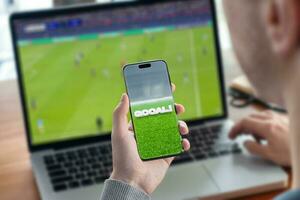 Guy watching football game on laptop and live score on smart phone concept photo