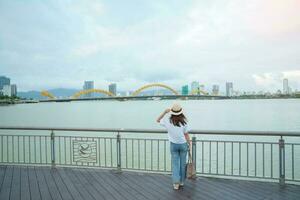 Woman Traveler visiting in Da Nang city. Tourist sightseeing the river view with Dragon bridge. Landmark and popular for tourist attraction. Vietnam and Southeast Asia travel concept photo