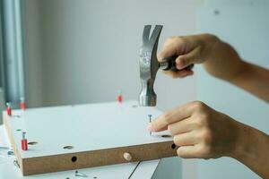 hombre usando un martillo clavando un clavo en tablas de madera, ensamblando o reparando muebles en casa. conceptos de bricolaje, renovación, reparación y desarrollo de viviendas o apartamentos foto