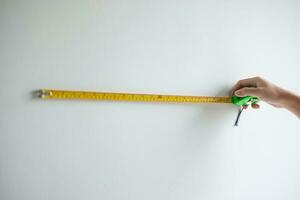 Man hand using tape measure for measuring with wall backgrounds at home. DIY, Interior design, repairing and improvement home or apartment concepts photo