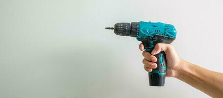 man hand holding cordless screwdriver with wall background, Carpenter working with electric screwdriver on the work photo