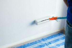 painter man with paint roller brush painting the wall. Renovation, maintenance and development of home or apartment photo