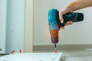 man using a cordless screwdriver assembling furniture at home, Carpenter working with electric screwdriver on the work photo