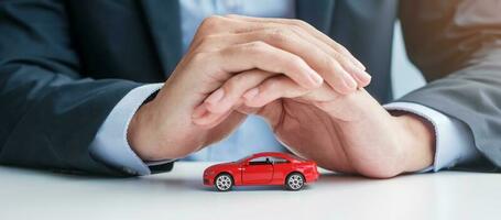 Businessman hand cover or protection red car toy on table. Car insurance, warranty, repair, Financial, banking and money concept photo