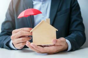 Businessman hand holding red Umbrella cover wooden Home model. real estate, insurance and property concepts photo