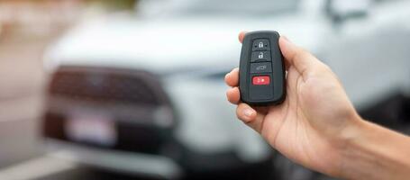 Hand holding car remote control, smart key to lock or unlock doors of white car. Safety, travel and transportation concept photo