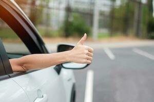 mujer mano pulgar hacia arriba durante la conducción de un coche en la carretera, mano controlando el volante en un automóvil eléctrico moderno. conceptos de transporte de viaje, viaje y seguridad foto